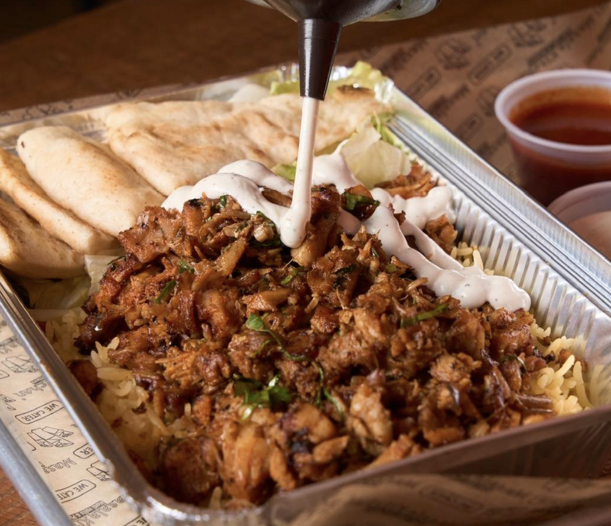 Platter of meat, rice and bread as someone pours sauce on top